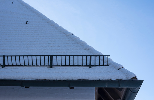 a metal snow guard fence at a roof in winter with snow covered tiles