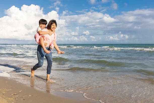 istock happy mother carrying her son on back and running on the beach 1403121054
