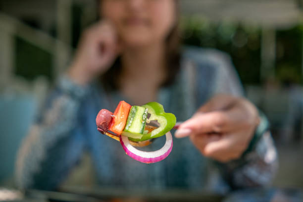 Woman holding fork with red onion, green pepper, cucumber, tomato and olive on it.
