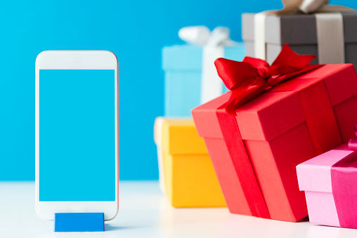 Multicolored gift boxes and a smart phone on white table in front of a blue wall.