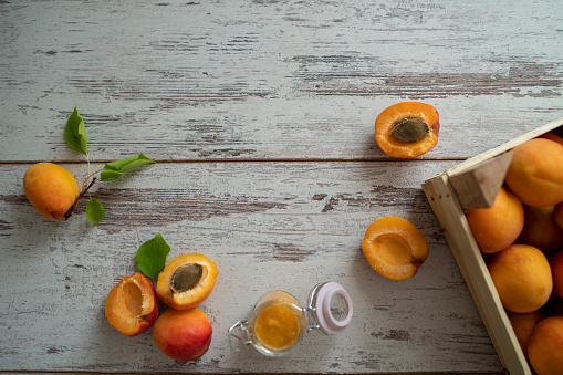 Female hands cutting fresh sweet peaches. Peaches whole fruits leaves, half peach, peach slices on white wooden kitchen table. Recipe making peach jam, cooking peach dessert on cutting board. Flat lay