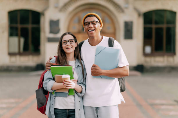 istock Two students standing together near the university, outdoors, looking at the camera. Two cheerful students, holding copybooks and folders 1403122860