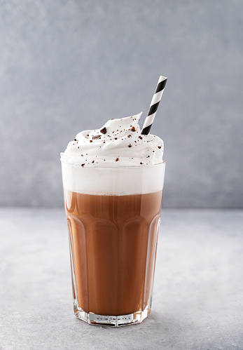 Hot chocolate with whipped cream in a tall glass on a blue background. Front view and copy space.