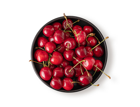 Fresh cherries in a black bowl on a white isolated  background. Top view and copy space.