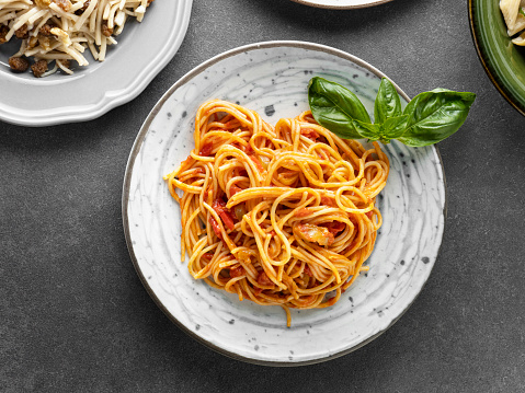 Italian lunch. Spaghetti alla puttanesca - italian pasta dish with tomatoes, olives, capers and parsley. Light background. Copy space.