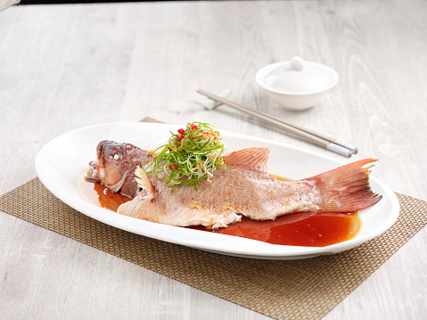 Steamed Star Grouper with Supreme Soya Sauce Served in a dish isolated on wooden board side view on grey background