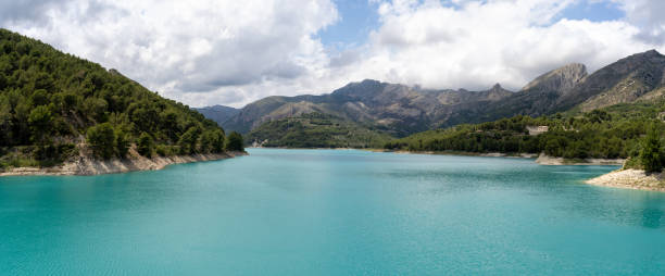 Panoramic view of a lake surrounded by pine forests with a sky with clouds Panoramic view of a lake surrounded by pine forests with a sky with clouds. Environmental conservation concept reservoir stock pictures, royalty-free photos & images