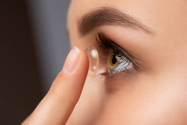 Beautiful woman holds contact lens on her finger. Eye care and the choice between the means to improve vision. stock photo