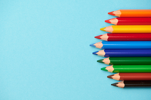 a row of colored pencils with different colors against light blue background, pencils on the right side with copy space