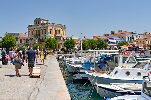 Aegina, Greece, - May 2022: People walking past small fishing boats after arriving by ferry at the harbour on the island of Aegina, which lies 17 miles of the coast of Athens