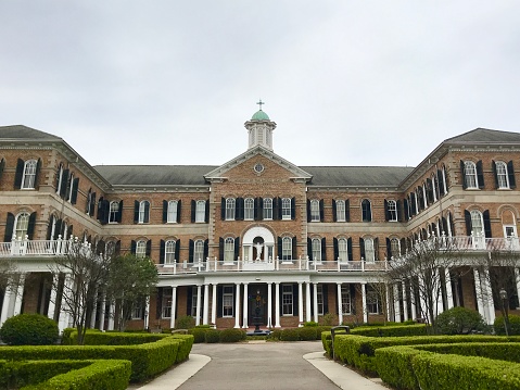 New Orleans, Louisiana State, USA - March 3, 2022: Academy of the Sacred Heart facade, New Orleans, Louisiana, USA United States of America.\n\nThe Academy of the Sacred Heart is a private Catholic high school in New Orleans, Louisiana. It is located within the Archdiocese of New Orleans and was established in 1886 by the Society of the Sacred Heart.\n\nThe traditional architecture suggests a respect for higher education and learning. Horizontal straight-on exterior view of an old red brick high school or elementary schoolhouse building facade, centered on the entrance front door and staircase.