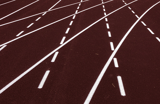 All-weather running track, white dash and solid lines crosses on brown rubber racetracks, selective focus. Racing curve on runner lanes surface, depth of field. Competition, pace abstract concept.