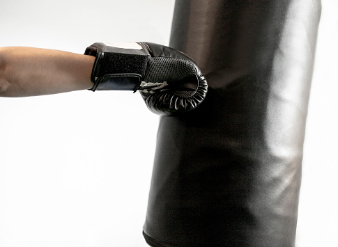 Box training, man's arm with black leather boxing glove punch direct to sandbag at the gym. Indoor sports activity for strength and physical health, isolated. Concept of fighter, challenge, professional