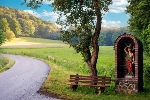 meadow with road and a christian wooden statue with bench
