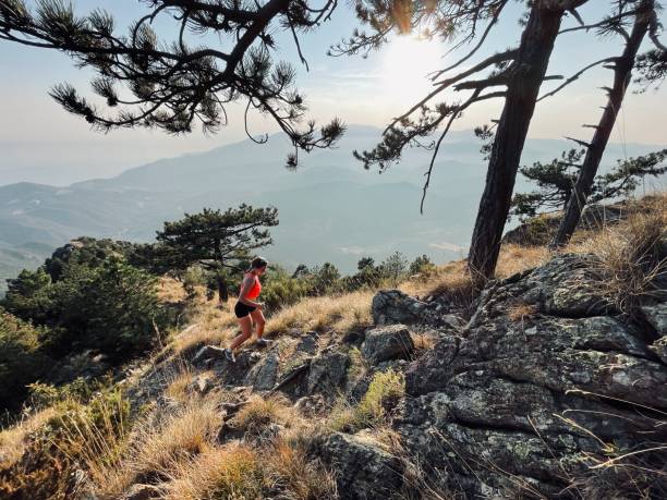 Young woman hikes up arid mountain side through forest