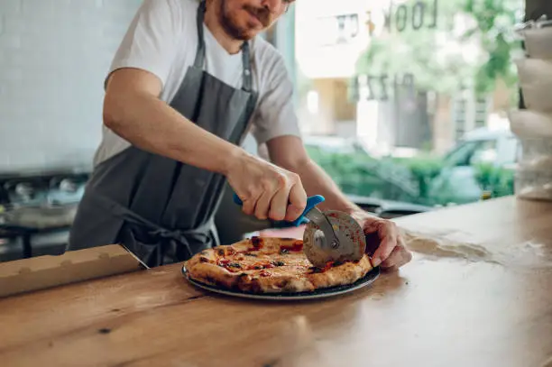 Photo of Hand of kitchen chef cutting pizza with a pizza cutter