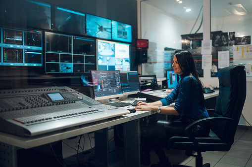 Middle aged beautiful woman working in a broadcast control room on a tv station. Entertainment news with footage equipment concept. Focus on a woman working in a broadcast room. Copy space.