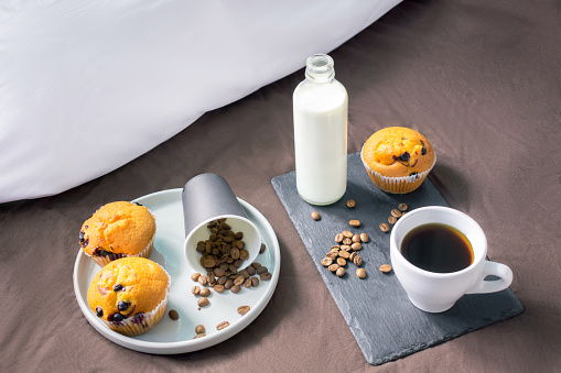 paper cup of coffee and milk in bottle on the bed with beans, muffins or cakes on plate as dessert for breakfast. Proper nutrition. stay safe home concept with copy space.