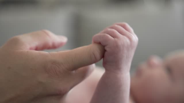 Newborn infant baby boy's hand holds onto mom's finger