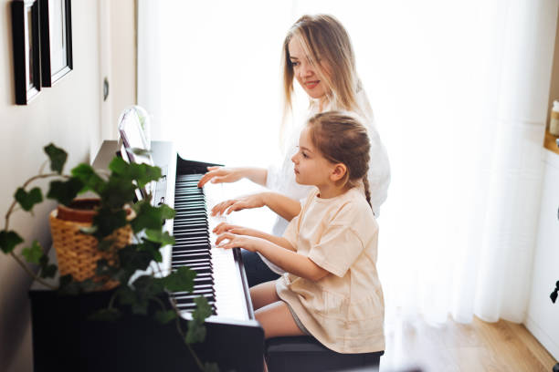 junge pianistenlehrerin, die schülerin klavier spielen beibringt, musikpädagogisches konzept - practicing piano child playing stock-fotos und bilder