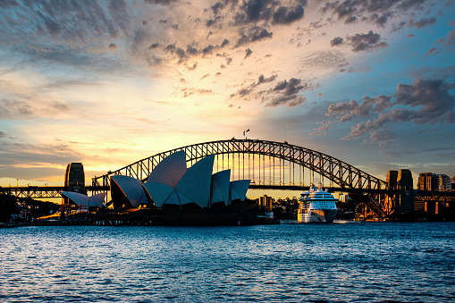 Color Photograph of the Sydney Opera House and Sydney Harbor Bridge at sunset with a cruise ship leaving Circular Quay