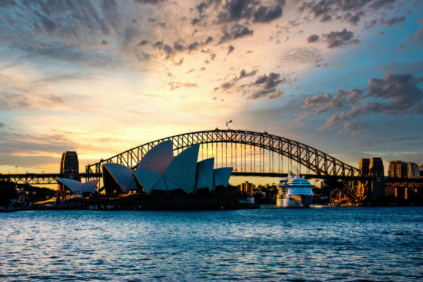 Sydney Opera House and Harbor Bridge at Sunset Color Photograph of the Sydney Opera House and Sydney Harbor Bridge at sunset with a cruise ship leaving Circular Quay sydney skyline sunset stock pictures, royalty-free photos & images