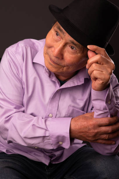 Dark studio background portrait of senior Vietnamese man wearing black hat.
