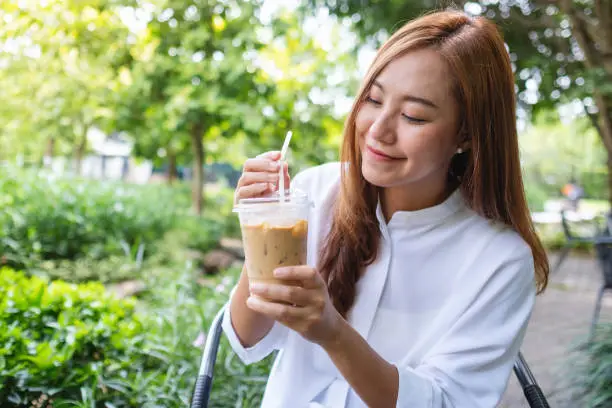 Photo of Portrait image a young asian woman holding and drinking iced coffee in the outdoors