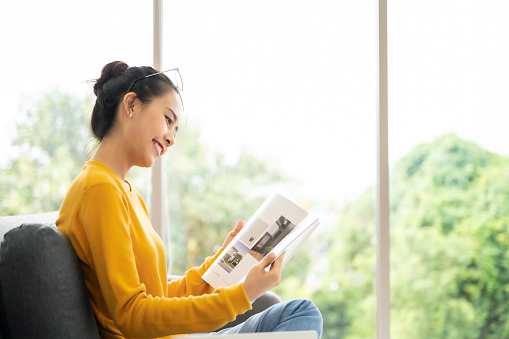 Happy young asian woman reading on the sofa in the living room at home