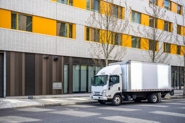 Small compact cab over truck with box trailer delivering cargo to multilevel urban city apartments stock photo