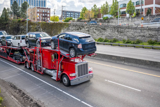 Red powerful big rig car hauler semi truck with loaded modular semi trailer driving on the highway road at the city limit going to point of destination stock photo