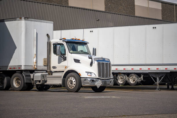 istock Day cab white big rig semi truck with dry van semi trailer unloading cargo standing in warehouse dock 1403174376