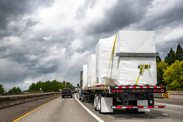 Powerful big rig semi truck tractor transporting heavy duty equipment on flatbed semi trailer driving on the multiline highway road with storm sky stock photo