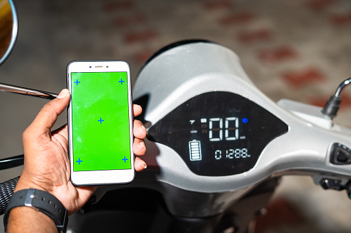 Close up shot of man hands showing green screen mobile phone near ev or electric scooter odometer - concept of online booking service, technology and transportation.