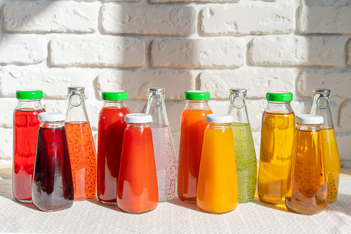 Row of glass bottles of different juices against white brick wall with shadows