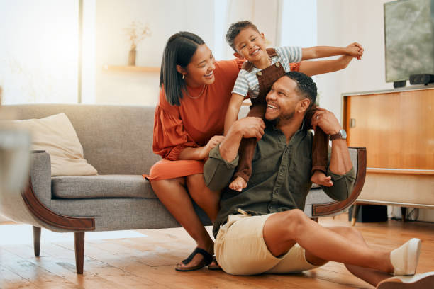 eine glückliche gemischtrassige familie von drei personen, die sich in der lounge entspannen und zusammen verspielt sind. liebe schwarze familie, die sich mit ihrem sohn verbindet, während sie zu hause lustige spiele auf dem sofa spielt - wohngebäude stock-fotos und bilder