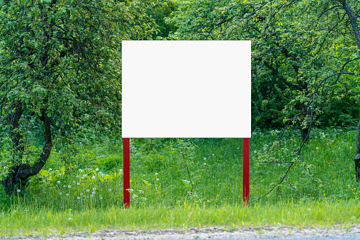 White empty signboard with space for mockup stands on summer garden. Information blank banner on nature background.