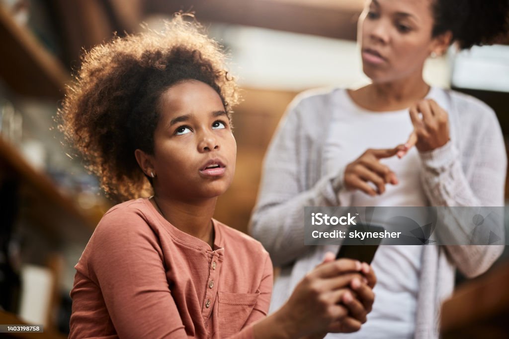 Oh my God, she is so annoying! Irritated African American girl using cell phone while ignoring her mother who is taking to her. Child Stock Photo