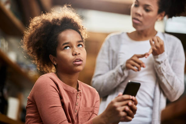 Oh my God, she is so annoying! Irritated African American girl using cell phone while ignoring her mother who is taking to her. rolling eyes irritation displeased facial expression stock pictures, royalty-free photos & images