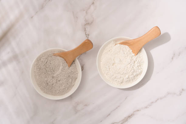 istock Top view on two white bowls with gray and white cosmetic clay on white marble table - mineral powder, bentonite facial mask. Skincare beauty concept. Selective focus 1403199930