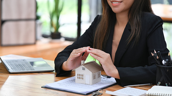 Female real estate agent hands sheltering house model. Real estate investment, property insurance and security concepts.