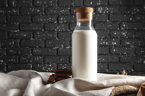 Glass bottle of milk and cookies on dark background, close up