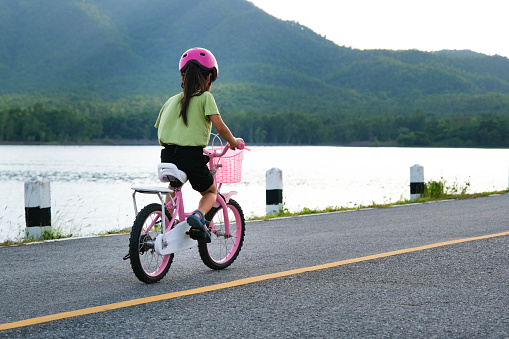 Cute little girl in a helmet riding a bicycle on an asphalt road in summer. Happy little girl riding a bicycle outdoors. Healthy Summer Activities for Kids