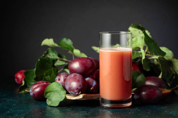 Glass of plum juice on a table with fresh purple plums. Copy space.