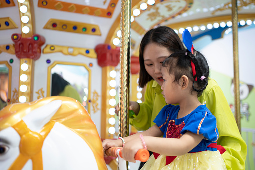 Happy little blond girl having fun riding horse on carousel amusement park ride in summer