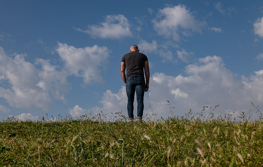 Full length of adult man standing on grass against cloudy sky