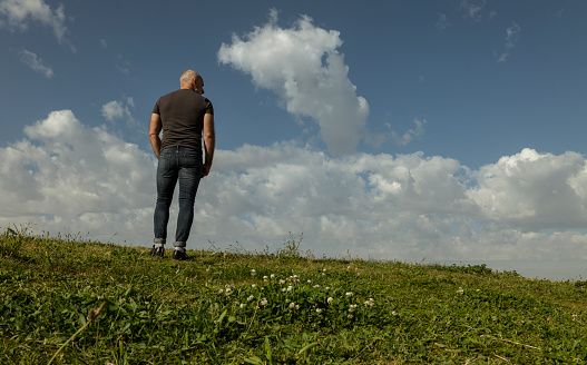 Full length of adult man standing on grass against cloudy sky