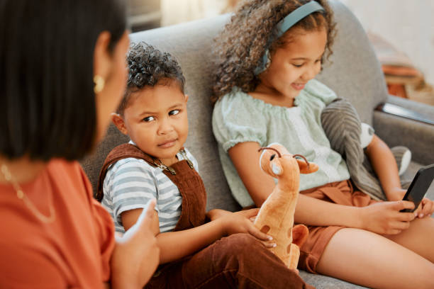 closeup of a mixed race single parent teaching her son a lesson about sharing while his sister is using a cellphone and headphones. a single parent putting her son in timeout for his bad behaviour - parent mother music listening imagens e fotografias de stock