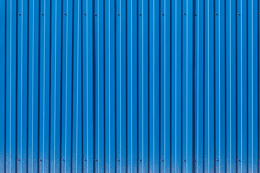 Fence made of blue profiled sheeting with mud splashes in the lower part