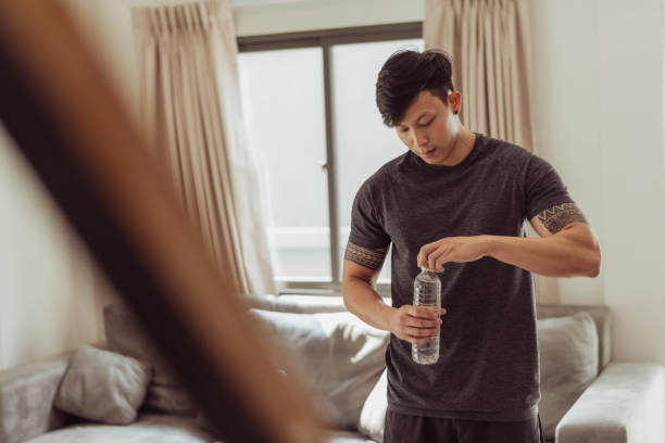 istock Fit man drinking water and take a break exercising at home. Young asian man resting after workout at home. 1403217382